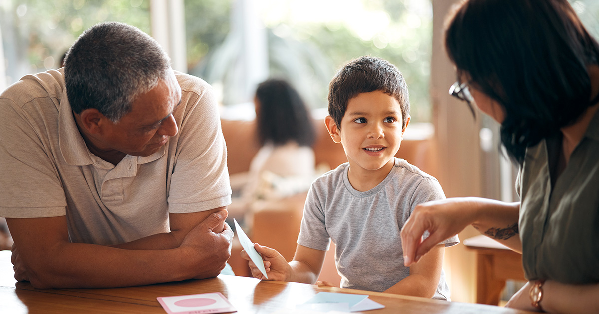 child sitting at a table with two adults holding a flash card